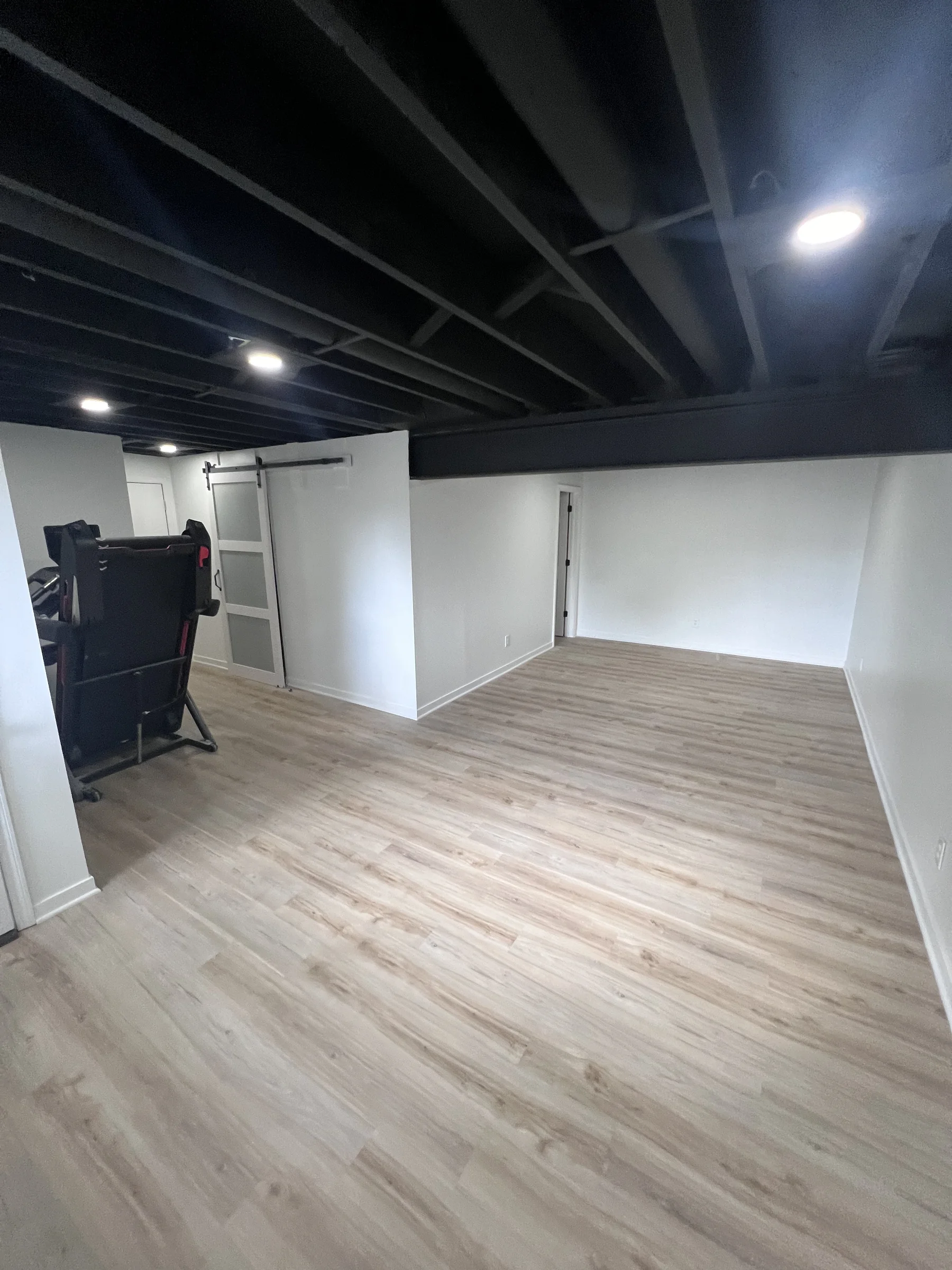 Finished basement with painted black ceiling, luxury vinyl plank floor and a barn door